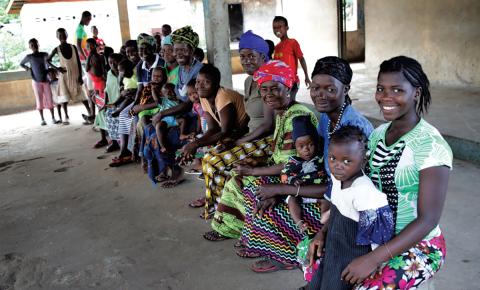 Mothers of Sierra Leone sit on a bench holding their children and smiling at the camera