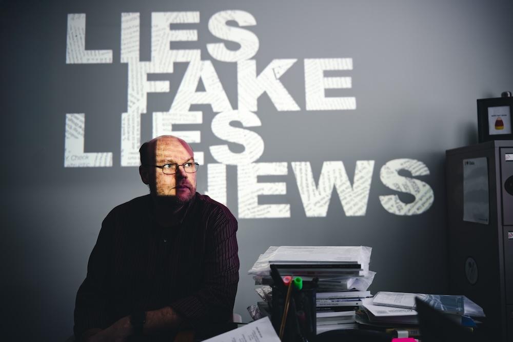 Jeremy Littau sits in front of words "Lies Fake News Lies" projected on the wall.